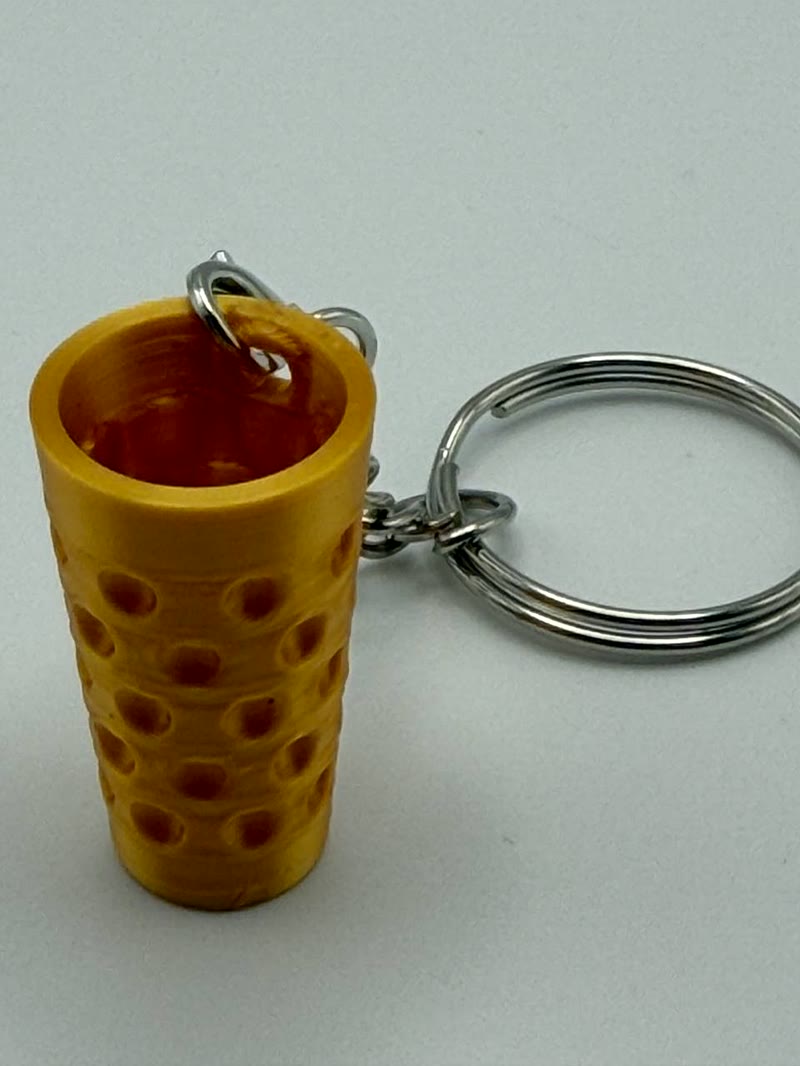 Echte Produktaufnahme eines goldfarbenen Dubbeglas-Schlüsselanhängers mit Befestigungsloch im oberen Rand